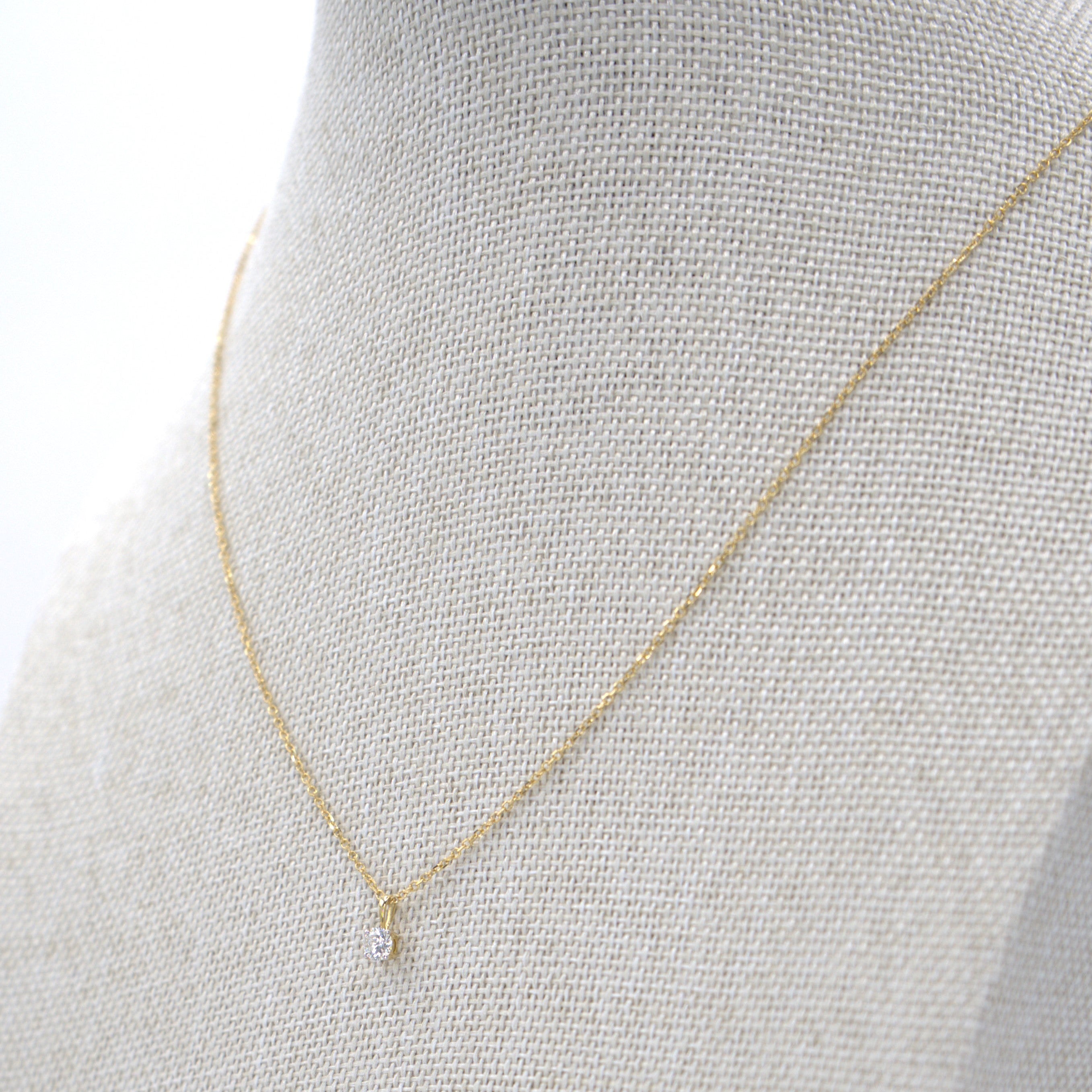 A yellow gold necklace with a round diamond pendant on a mannequin bust